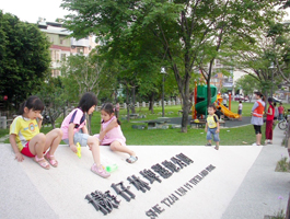 小女孩們喜歡坐在寫有「檨仔林埤濕地公園」字樣的三角錐形水泥碑從上往下滑，像玩溜滑梯。(圖/蕭夙茗攝)